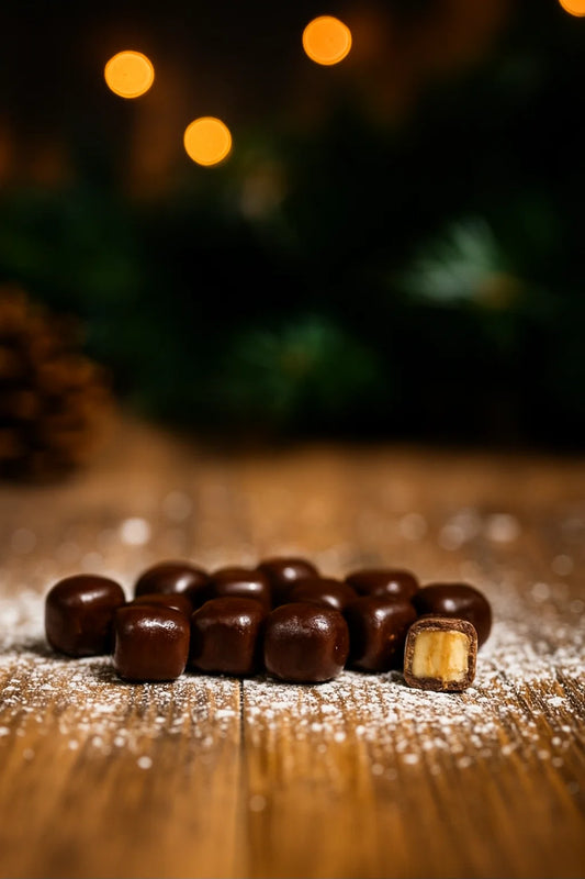 Chocolate covered caramel candies on wooden surface with pinecones and blurred Christmas lights